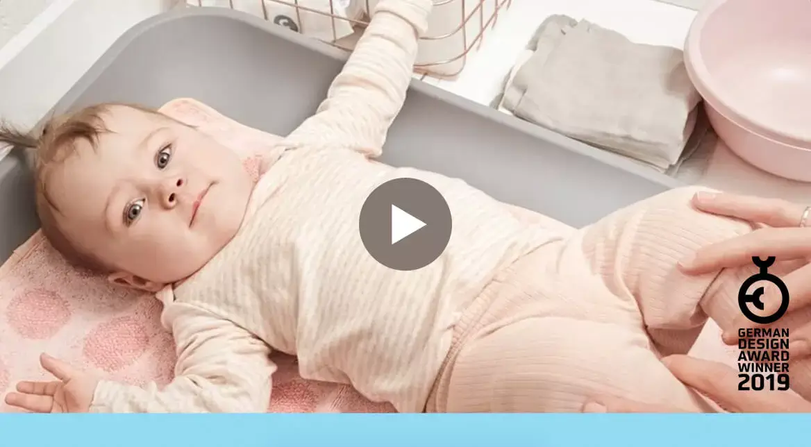 Baby laying on grey changing mat with pink towel and accessories