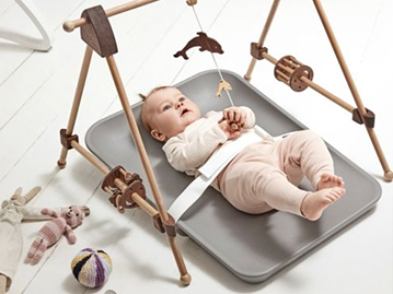 Baby laying on grey changing mat on the floor with safety belt attached playing with mobile