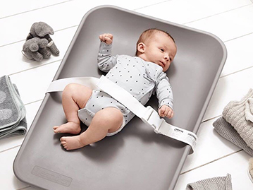 Baby laying on grey changing mat on the floor with safety belt attached